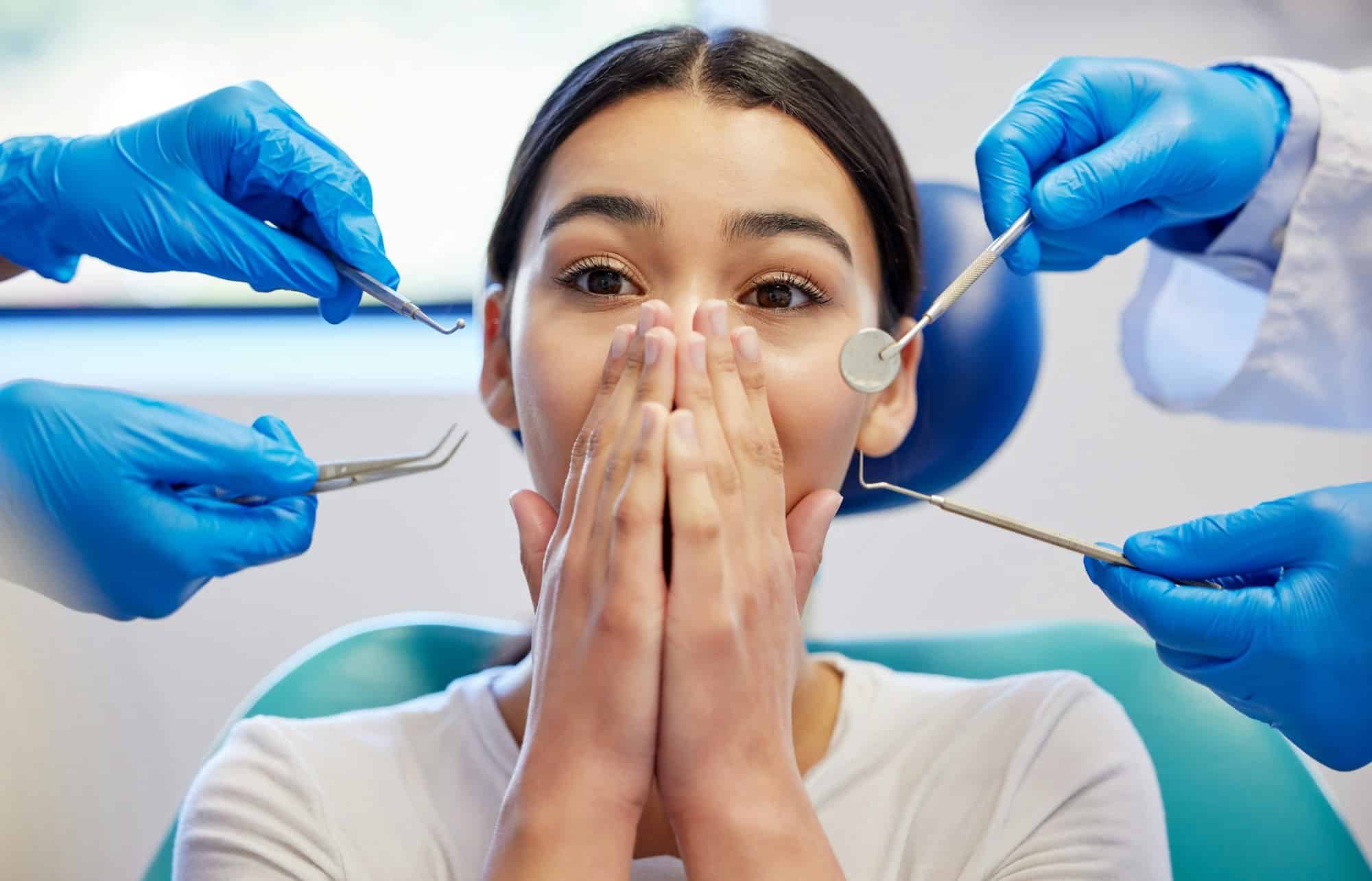 Anxious young woman covering her mouth in a dental chair as dentists attempt to examine her teeth, highlighting dental anxiety at Mayfair Family Dentistry.