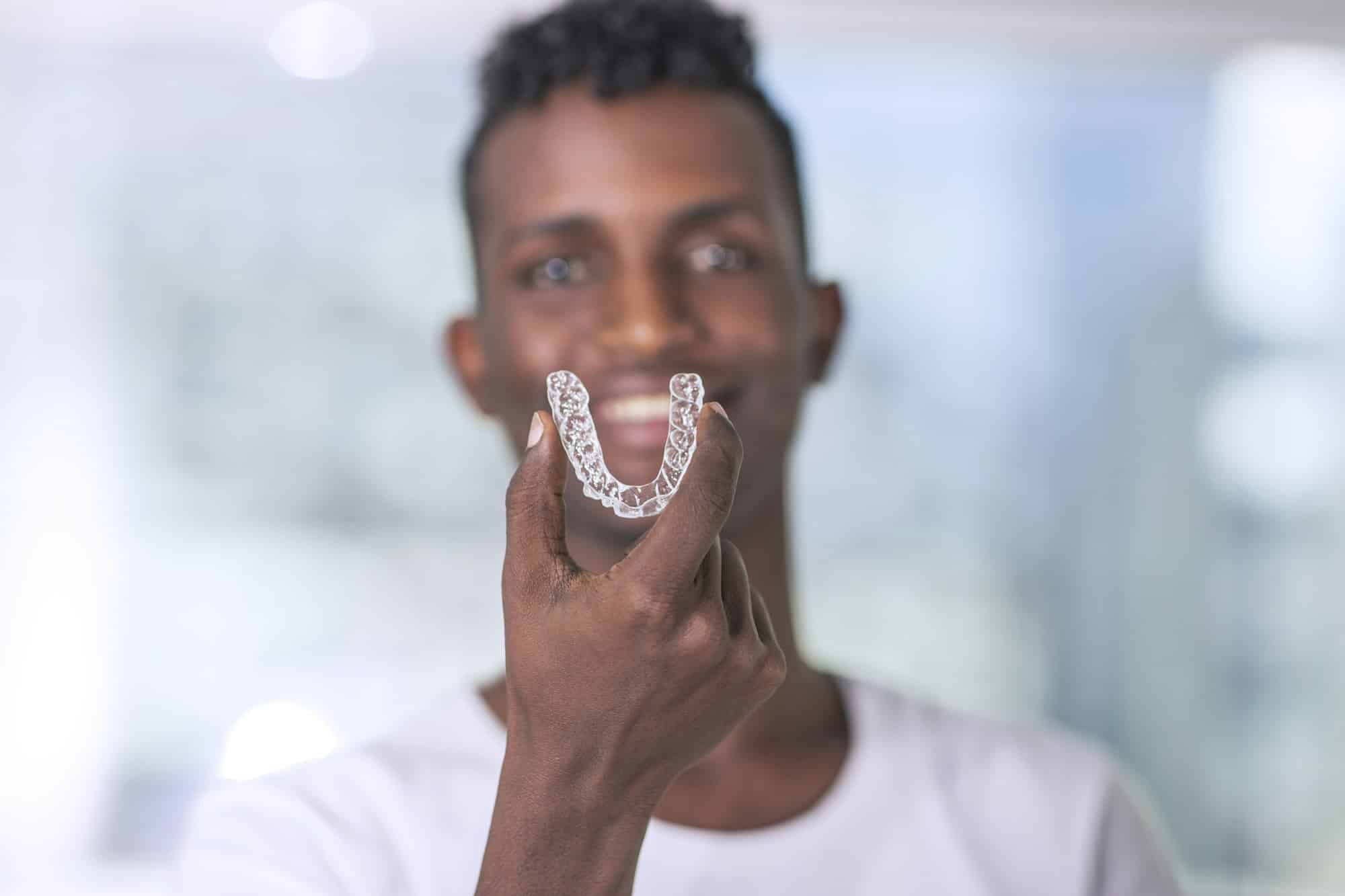 Close-up of a man inserting a top Invisalign aligner into his mouth at Mayfair Family Dentistry in Philadelphia.